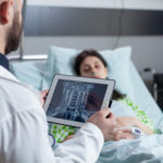 medic holding digital tablet with throat mri looking at sleeping patient in hospital bed e1700022743604